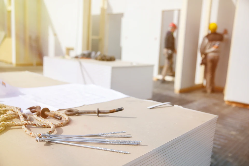 Chantier de construction intérieur avec ouvriers en arrière-plan portant casques de sécurité, travaillant dans un espace résidentiel en rénovation