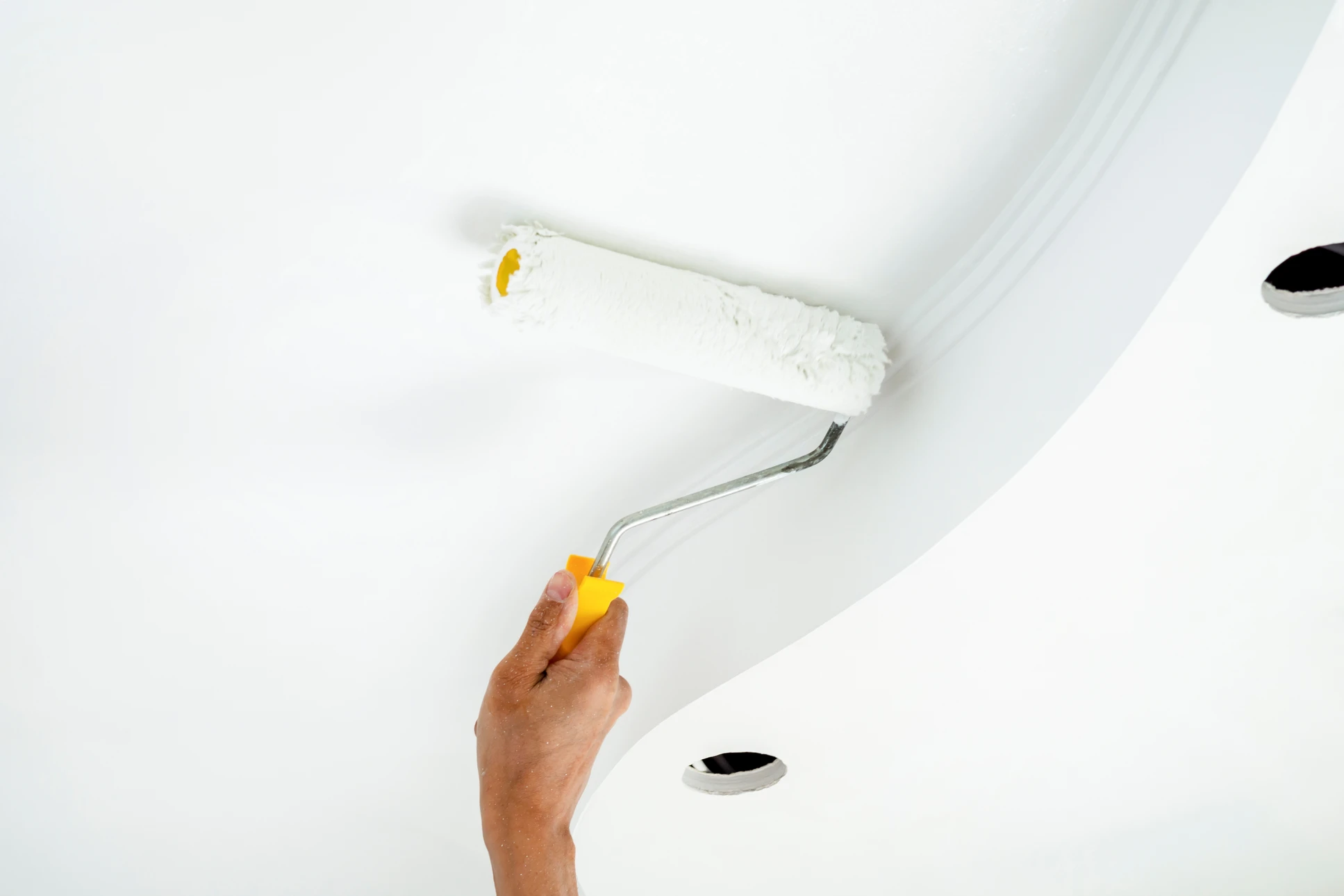 Peintre professionnel sur échelle appliquant de la peinture blanche sur bardage extérieur d'une maison à deux étages