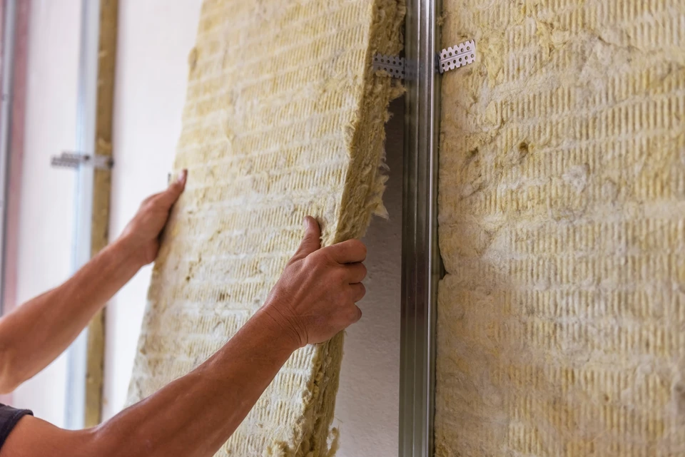 Ouvrier en salopette verte installant de l'isolant thermique en laine de verre jaune entre les solives d'un plancher en construction